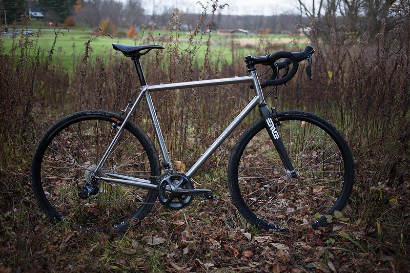 A black and grey cyclocross bike is in the bush, and autumn leaves 